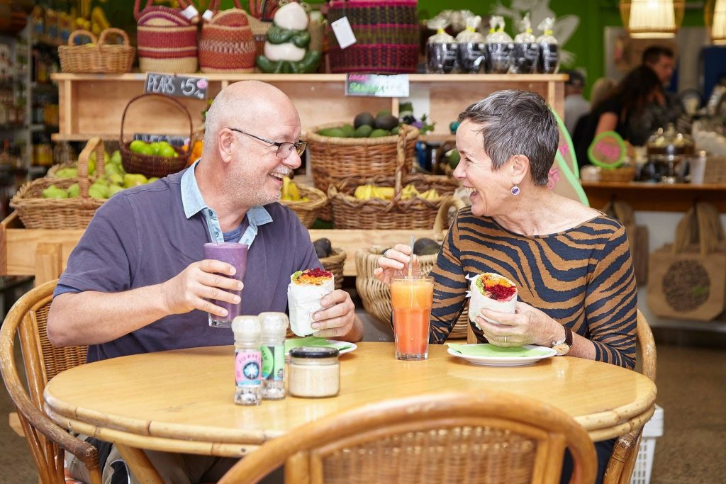 Man and woman sitting at cafe table eating salad wraps with fresh juice and smoothie