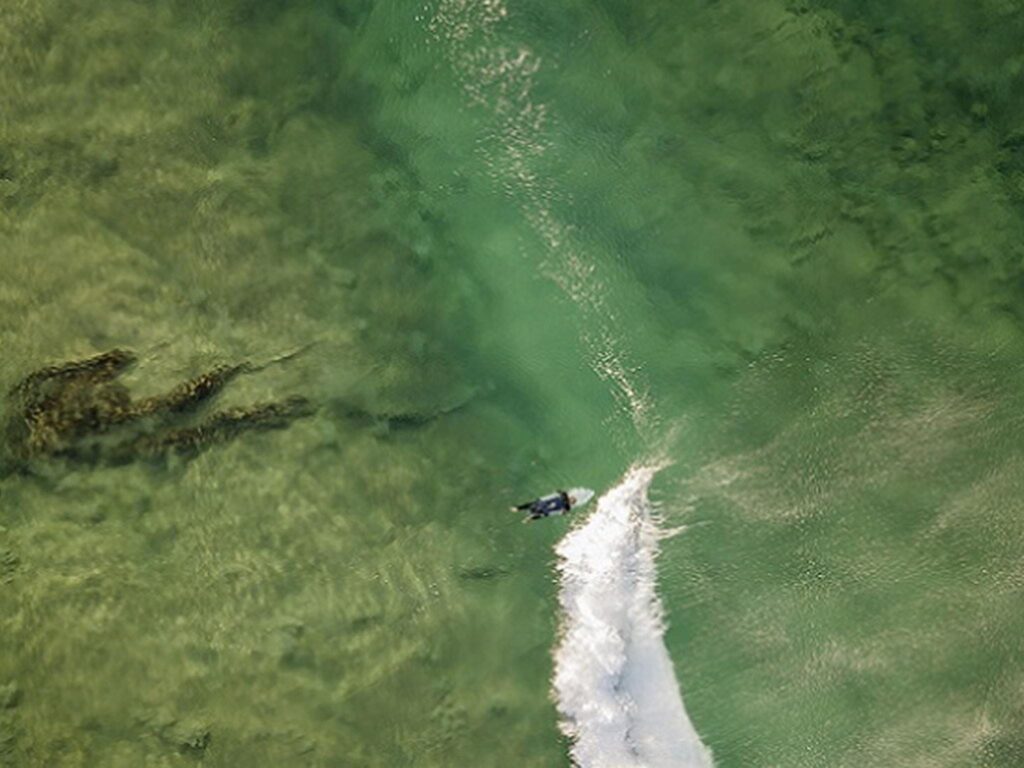 Aerial view of surfer in the water close to Tuckers Rocks Cottage. Photo: John Spencer/DPIE