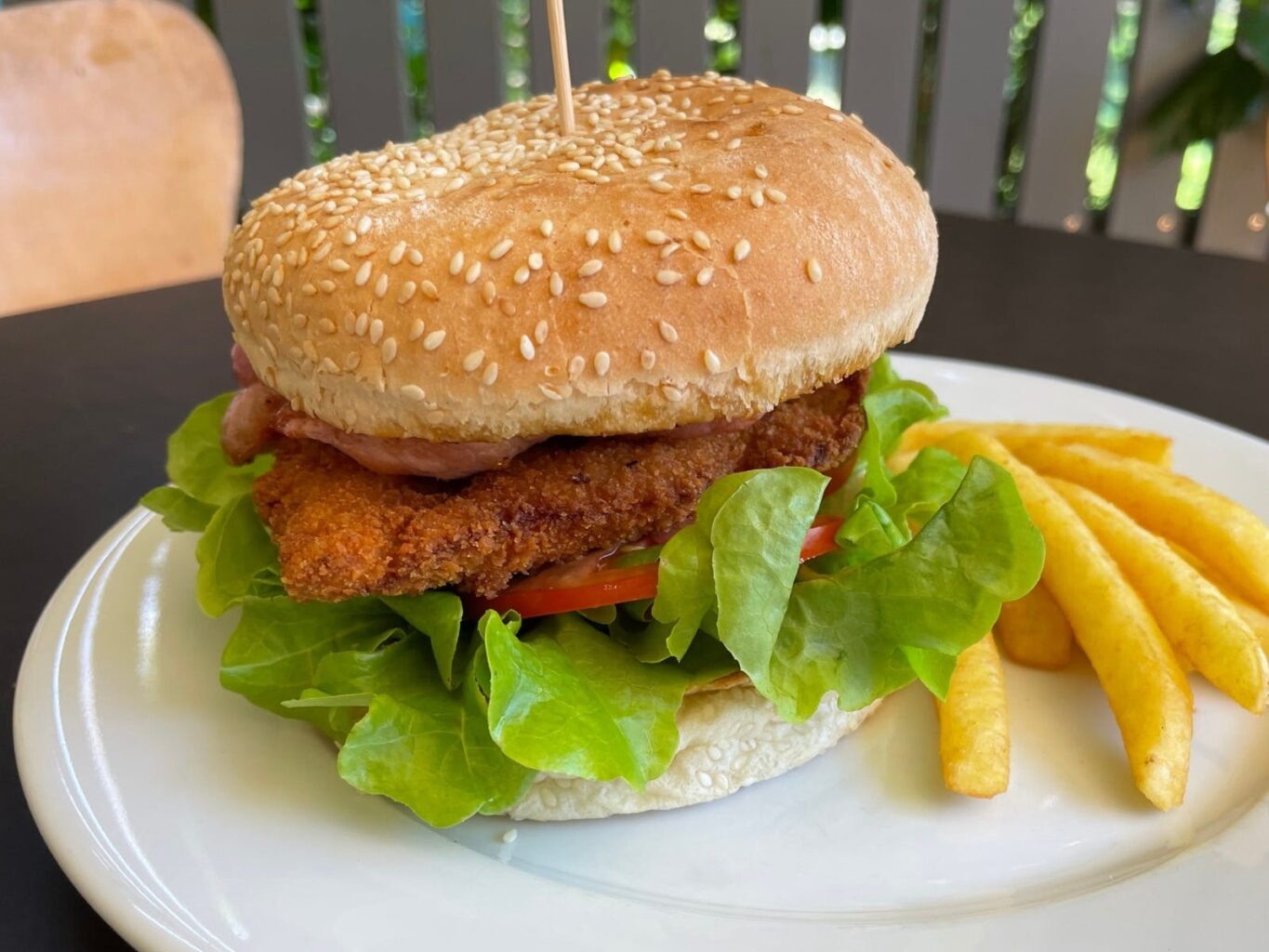 Chicken & bacon burger on a sesame seed bun served on a plate with salad and chips