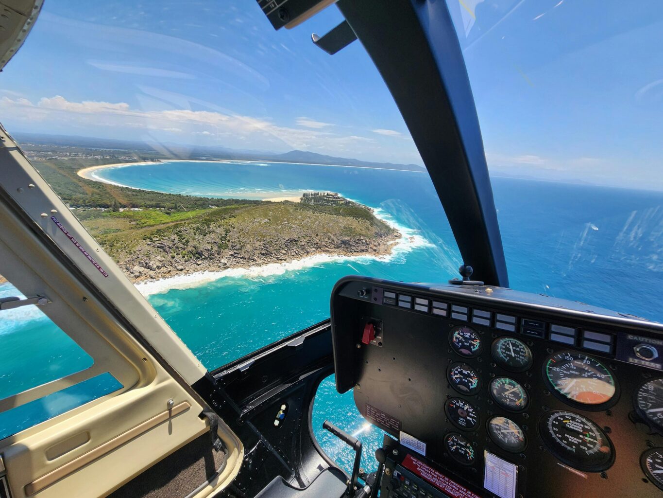 View from a Helicopter of the Coffs Coast with a headland, blue ocean, white sand, rugged terrain